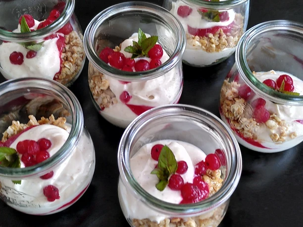 Johannisbeer-Dessert Sechs Dessertgläser mit joghurtbasiertem Dessert, garniert mit roten Beeren und frischer Minze.