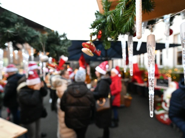 OWN_5607.JPG Eiszapfen und grüne Tannenzweige hängen an einer Holzhütte auf dem Weihnachtsmarkt. Im Hintergrund erkennt man verschwommene Umrisse von Menschen mit roten Weihnachtsmannmützen