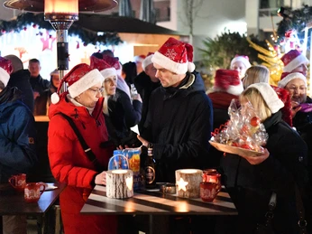 Piccolo Event Company GmbH Menschengruppe steht mit roten Weihnachtsmannmützen an kleinen Stehtischen auf dem WeihnachtsmarktGroup of people wearing red Santa hats standing at small bar tables at the Christmas market