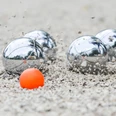 Boule-Foto-Internet.png Vier silberne Boulekugeln und eine kleine orangefarbene Zielkugel auf kiesigem Boden