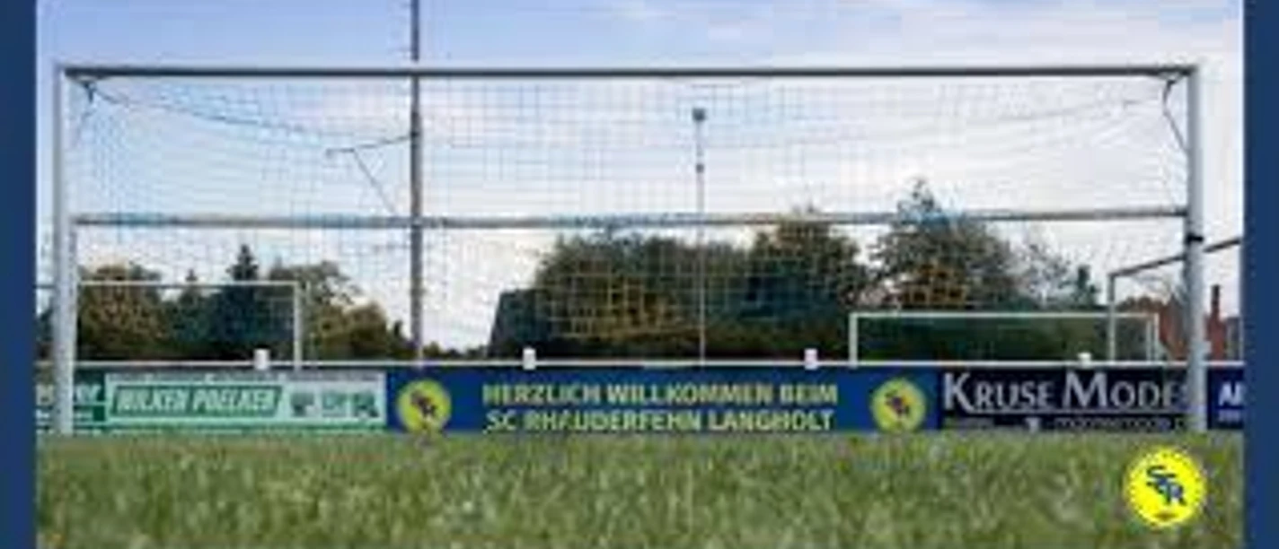 Sportanlage_SC Rhauderfehn_ Langholt Fußballtor mit Netz auf einem Spielfeld, Werbebanner mit Text 'Herzlich Willkommen beim SC Rhuderfehn Langholt' und Firmenlogos im Hintergrund.