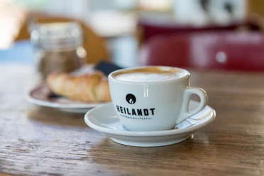 Cafe Heilandt Nahaufnahme einer Tasse Cappucchino und Croissant.