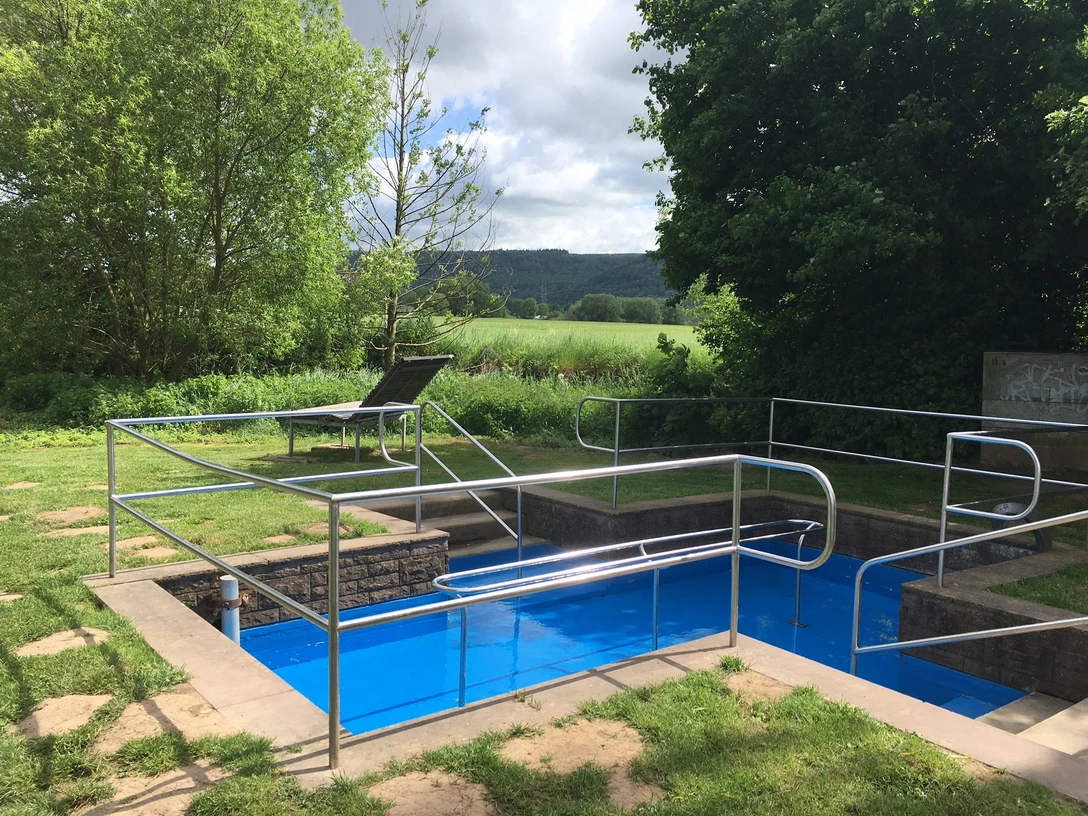 Kneipptretbecken Beverungen Kneipptretbecken mit Wasser gefüllt, umlaufend ein Handlauf aus Metall, umgeben von Rasenfläche und Bäumen und einer Ruheliege