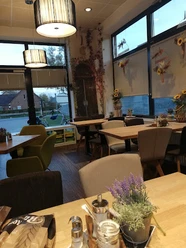 Bäckerei Ripken_Edeka_Augustfehn_2022.jpg The interior of the Ripken bakery in Augustfehn exudes a cozy and inviting atmosphere. Wood-paneled furniture and subtle decorations, such as dried flowers and modern lamps, create a stylish, rustic ambience. Large windows provide plenty of natural light and open up the view of the surroundings, while the table decorations with small pots of herbs underline the rustic charm.