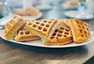 Ein Teller mit frisch gebackenen Waffeln, übereinander gestapelt und mit Puderzucker bestäubt.