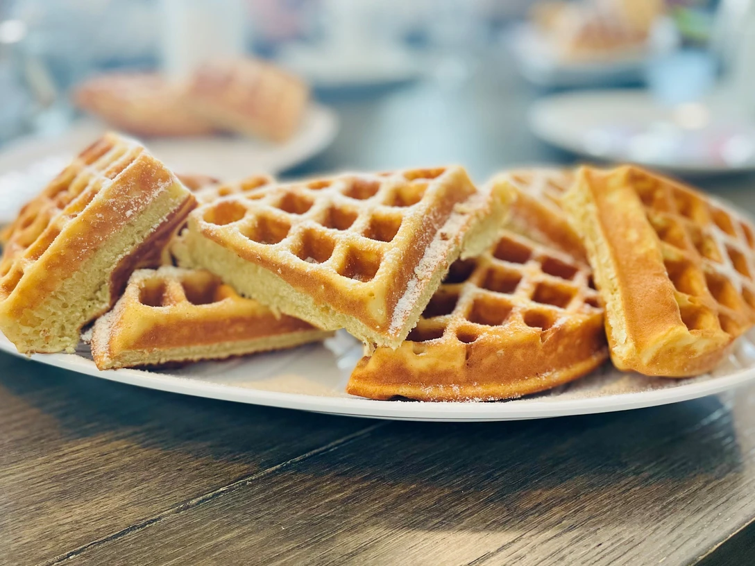 Ein Teller mit frisch gebackenen Waffeln, übereinander gestapelt und mit Puderzucker bestäubt.