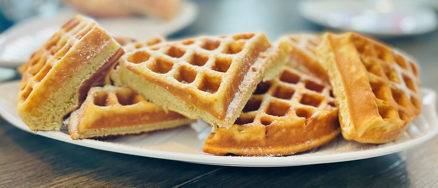 Ein Teller mit frisch gebackenen Waffeln, übereinander gestapelt und mit Puderzucker bestäubt.
