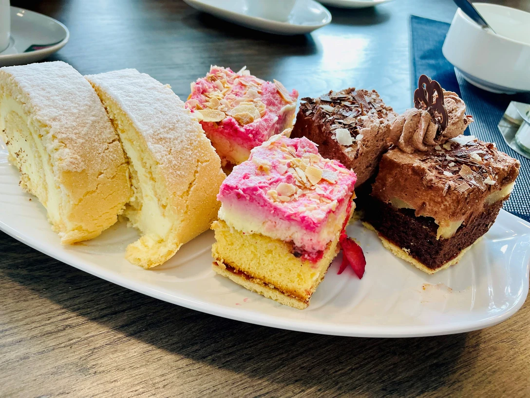 Kuchen_1_CC_BY_SA_Teutoburger_Wald_Stadt_Schloss_Holte-Stukenbrock.jpg Assortierte Kuchenauswahl auf weißem Teller, darunter Sahnerolle, fruchtiger Biskuitkuchen und Schokoladenschnitten.