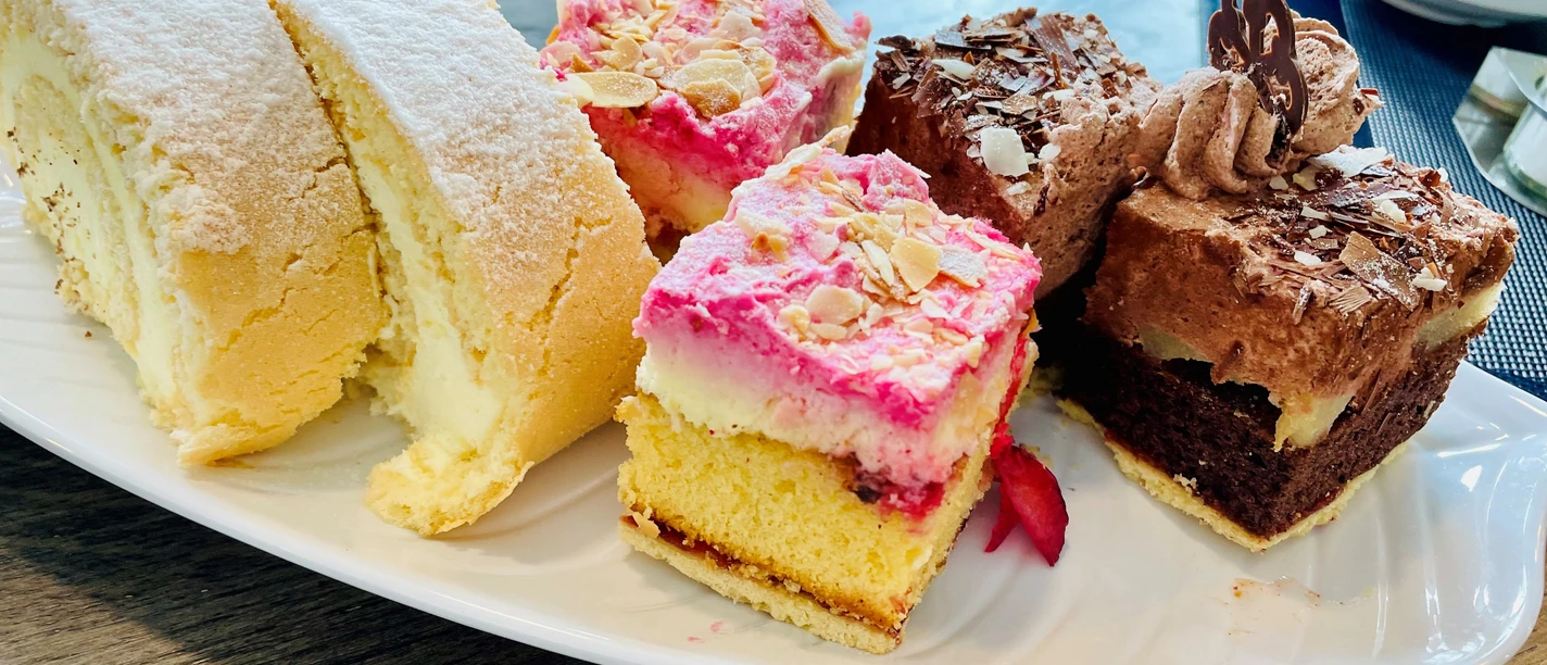 Kuchen_1_CC_BY_SA_Teutoburger_Wald_Stadt_Schloss_Holte-Stukenbrock.jpg Assortierte Kuchenauswahl auf weißem Teller, darunter Sahnerolle, fruchtiger Biskuitkuchen und Schokoladenschnitten.