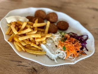Ein Teller mit Pommes, Falafel, Krautsalat und Saucen auf einem holzfarbenen Untergrund.