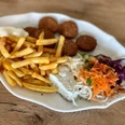 Ein Teller mit Pommes, Falafel, Krautsalat und Saucen auf einem holzfarbenen Untergrund.