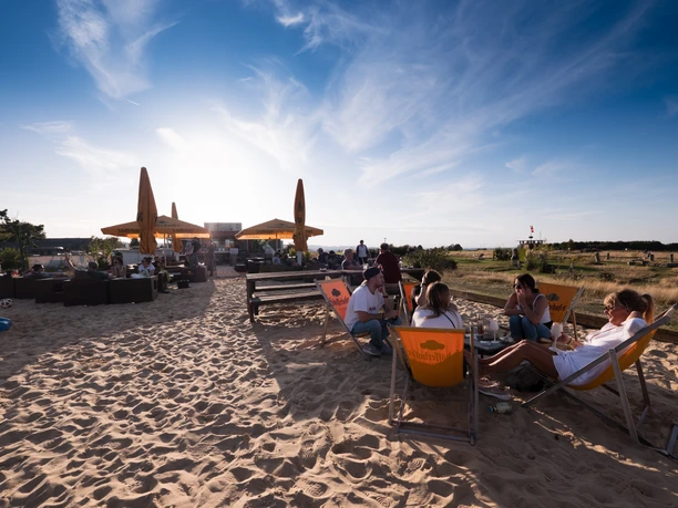 Beachbar Soccerpark Detmold Strandatmosphäre im Soccerpark Detmold mit Gästen in Liegestühlen unter Sonnenschirmen bei Sonnenuntergang.