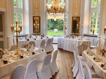 97d28a5d-915c-41d6-b024-fc9b7e3a686b.jpg Kleiner Raum im Barockstil mit weiß eingedeckten und festlich dekorierten TischreihenSmall room in Baroque style with rows of tables covered in white and festively decorated