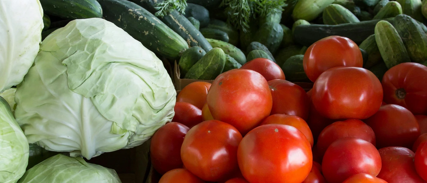 Frisches Gemüse mit Tomaten, Kohl, Zucchini und Möhren auf einem belebten Marktstand ausgebreitet.