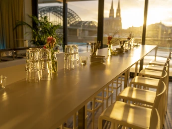 THE VIEW Hochtische Über die lange, dekorierte Tischreihe aus dem Panoramafenster fotografiert: Blick auf den Dom in der AbendsonnePhotographed through the panoramic window across the long, decorated row of tables: view of the cathedral in the evening sun.