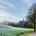 Klosterlandschaft Altenberg Kloster mit gotischer Fassade, umgeben von herbstlichen Bäumen und einer von morgendlichem Frost bedeckten Wiese.