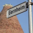 Gernheim Straßenschild.jpg Straßenschild mit der Aufschrift "Gernheim" vor einem historischen Ziegelturm und klarem Himmel.