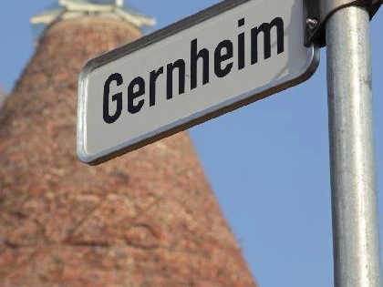 Gernheim Straßenschild.jpg Straßenschild mit der Aufschrift "Gernheim" vor einem historischen Ziegelturm und klarem Himmel.