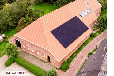 Kultur-Gulfhof-Freepsum Backsteingebäude mit rotem Ziegeldach und Solaranlage, umgeben von Grünflächen und Pflasterweg.