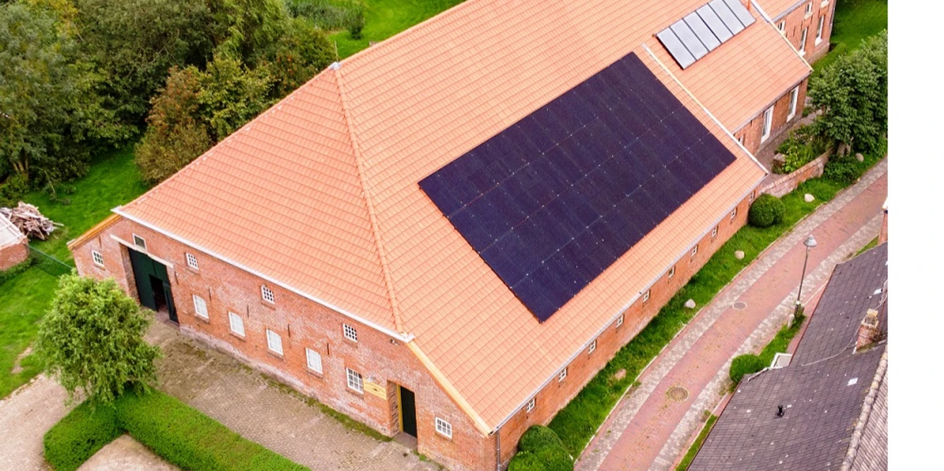 Kultur-Gulfhof-Freepsum Backsteingebäude mit rotem Ziegeldach und Solaranlage, umgeben von Grünflächen und Pflasterweg.