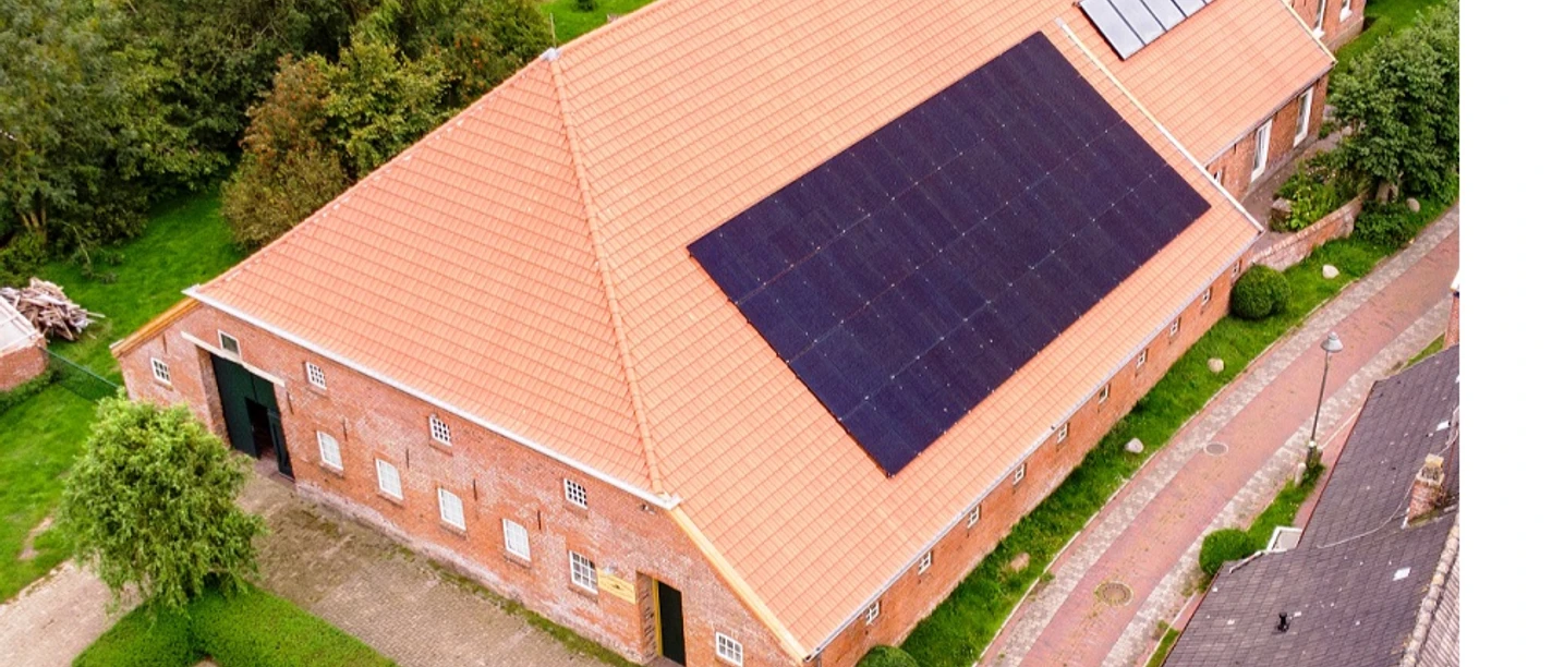 Kultur-Gulfhof-Freepsum Backsteingebäude mit rotem Ziegeldach und Solaranlage, umgeben von Grünflächen und Pflasterweg.