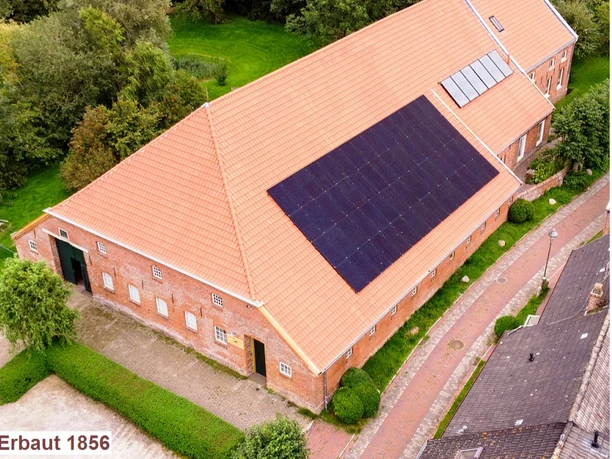 Kultur-Gulfhof-Freepsum Backsteingebäude mit rotem Ziegeldach und Solaranlage, umgeben von Grünflächen und Pflasterweg.