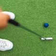 Adventure Golf Minigolfspieler trifft mit einem Putter auf einen blauen Ball auf grünem Kunstrasen.
