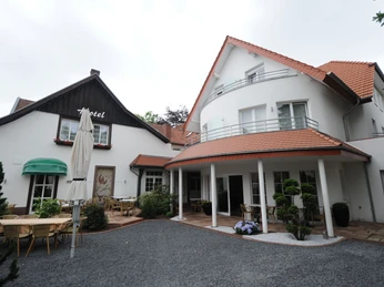 Außenansicht Isselhorster Landhaus Außenansicht eines Landhotels mit Terrassenbereich, mehreren Sitzgruppen und rotem Ziegeldach.