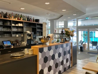 nostimo_3.jpg Moderner Gastronomietresen in Grautönen und Holzoptik und Regal mit Gläsern im Hintergrund