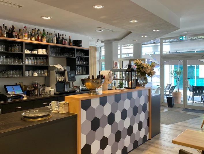 nostimo_3.jpg Moderner Gastronomietresen in Grautönen und Holzoptik und Regal mit Gläsern im Hintergrund