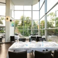 Restaurant Jordans Das Bild zeigt die moderne Innenansicht des Restaurants Jordans mit großen Glasfenstern, die viel Tageslicht hereinlassen und einen Blick ins Grüne ermöglichen. Die Einrichtung besteht aus eleganten schwarzen Stühlen und weißen Tischen, die in einem offenen und stillvollen Ambiente angeordnet sind.