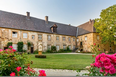 Teutoburger Wald, Klosteranlage Herzebrock, M. Wallenfang Historisches Schloss mit Rosengarten und Statuen, umgeben von grüner Landschaft und blauer Himmel.
