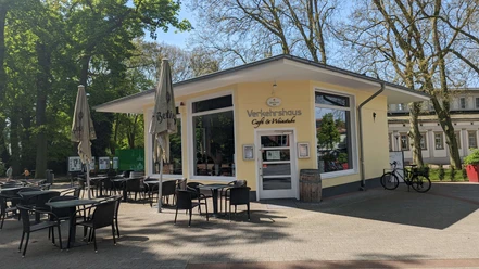 Verkehrshaus Seite Auf dem Bild ist die Außenansicht des Cafés zu sehen, das mit einer gelben Fassade bedeckt. Vor der Terrasse stehen gemütliche Tische und Stühle, die dazu einladen, die Sonne zu genießen.