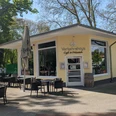 Verkehrshaus Seite Auf dem Bild ist die Außenansicht des Cafés zu sehen, das mit einer gelben Fassade bedeckt. Vor der Terrasse stehen gemütliche Tische und Stühle, die dazu einladen, die Sonne zu genießen.