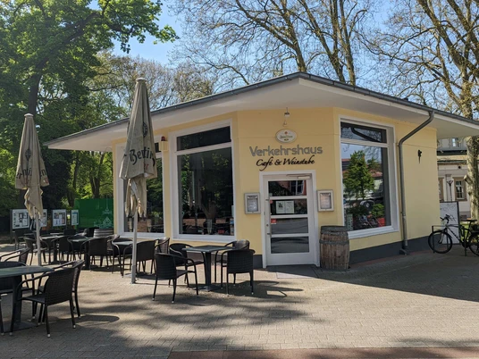 Verkehrshaus Seite Auf dem Bild ist die Außenansicht des Cafés zu sehen, das mit einer gelben Fassade bedeckt. Vor der Terrasse stehen gemütliche Tische und Stühle, die dazu einladen, die Sonne zu genießen.