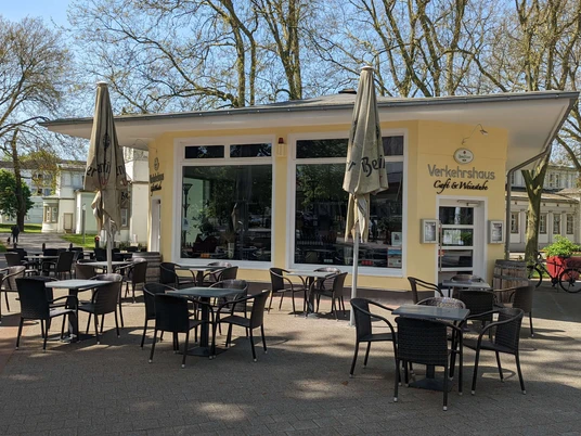 Verkehrshaus Auf dem Bild ist die Außenansicht des Cafés zu sehen, das mit einer gelben Fassade bedeckt ist. Vor der Terrasse stehen gemütliche Tische und Stühle, die dazu einladen, die Sonne zu genießen