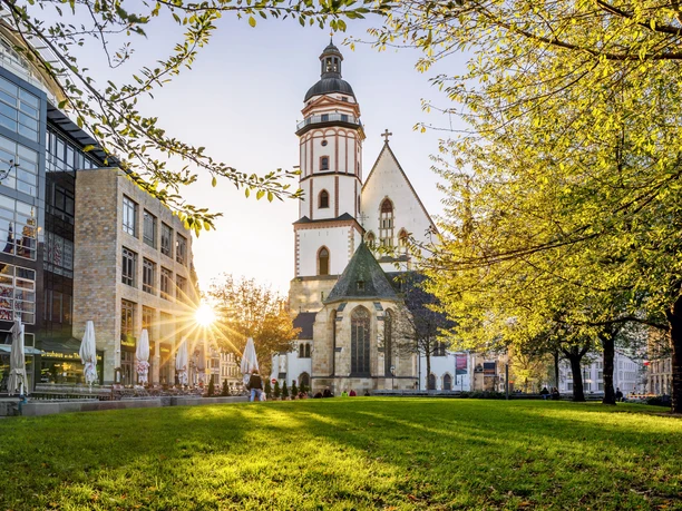 Vue de la verte Thomaswiese sur l'église Saint-Thomas au coucher du soleil, avec à gauche la brasserie de l'église Saint-Thomas et à droite des arbres, Leipzig, ville de musique, curiosités touristiques