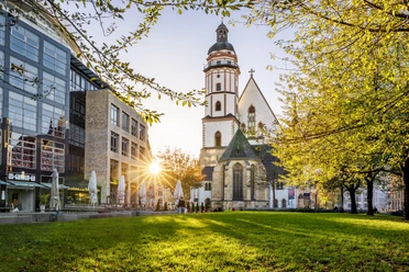 Widok z zielonego Thomaswiese na kościół Thomaskirche o zachodzie słońca, po lewej browar przy kościele Thomaskirche, a po prawej drzewa, Miasto Muzyki Lipsk, Ciekawe miejsca