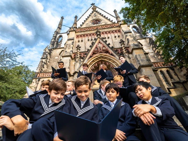 Les enfants du Thomanerchor sont assis et debout en costume devant l'église Saint-Thomas de Leipzig et regardent leurs cahiers de chant, Leipzig, ville de musique, culture
