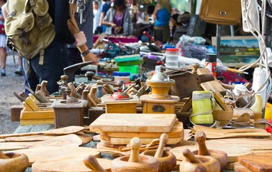 Marktstand mit handgefertigten Holzprodukten und Antiquitäten, Menschen im Hintergrund.