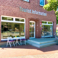 Tourist-Information Ein rotes Backsteingebäude mit der Aufschrift "Tourist Information". Ein Tisch und zwei Stühle stehen vor dem Eingang.