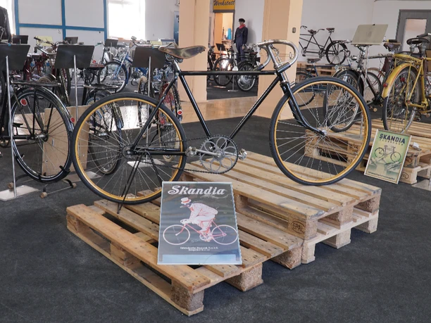 Bismarck Ausstellung Eine Ausstellung mit historischen Fahrrädern, darunter ein elegantes schwarzes Rennrad auf Holzpaletten.