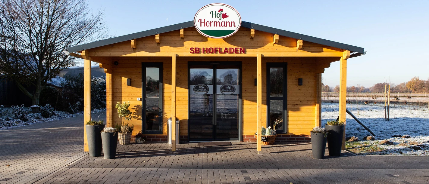 Hofladen Außen.jpg Ein kleiner, rustikaler Selbstbedienungs-Hofladen aus Holz in ländlicher Umgebung mit Winterhintergrund.