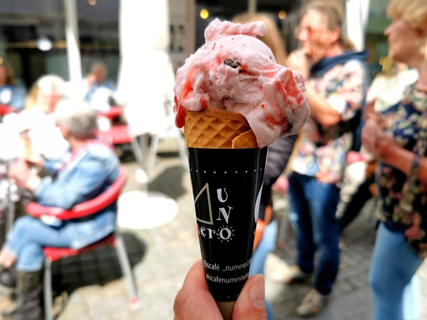 Kulinarische Stadtführung "Günzburg zum Probieren" Eis in einer Waffel mit Fruchteiscreme, gehalten von einer Person, im Hintergrund Menschen in lockerer Unterhaltung.