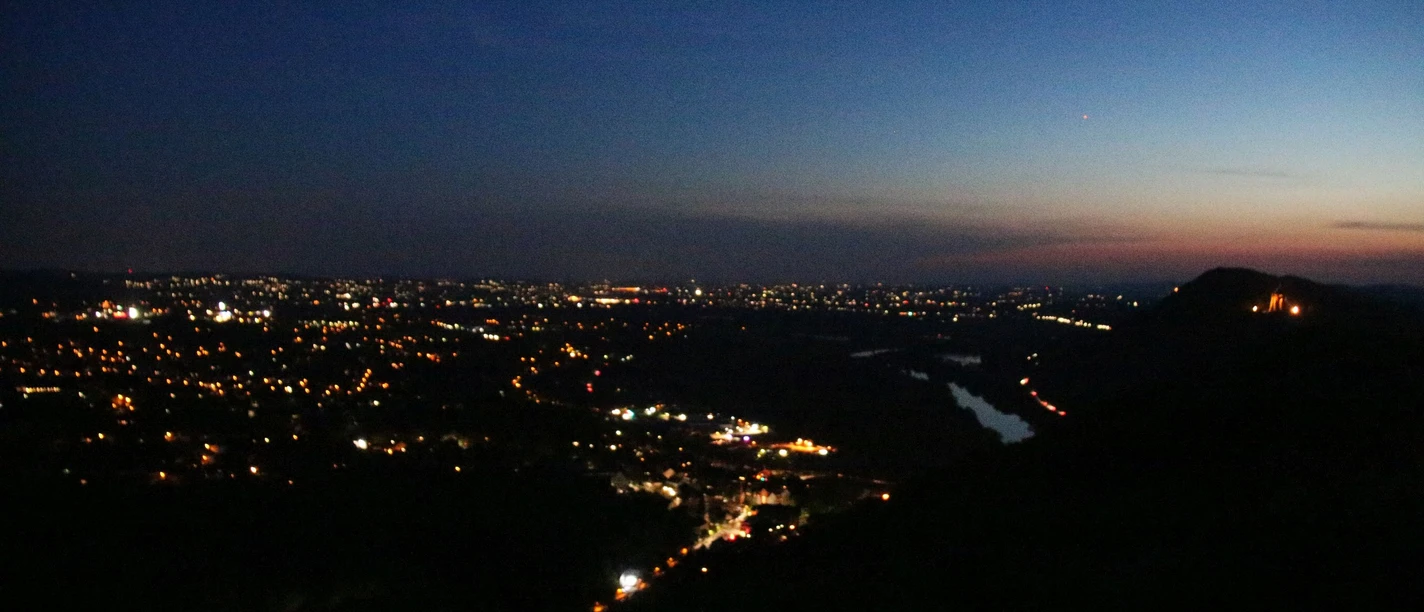 Nächtliche Skyline mit leuchtenden Stadtlichtern und einem Fluss, der durch das dunkle Tal fließt.