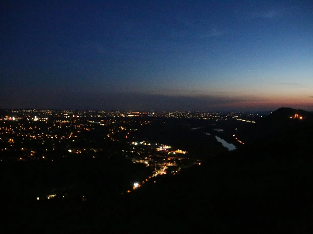 Nächtliche Skyline mit leuchtenden Stadtlichtern und einem Fluss, der durch das dunkle Tal fließt.