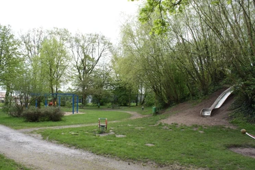 Ein Abenteuerspielplatz mit blauer Kletteranlage, grüner Umgebung und silberner Rutsche am Waldrand.