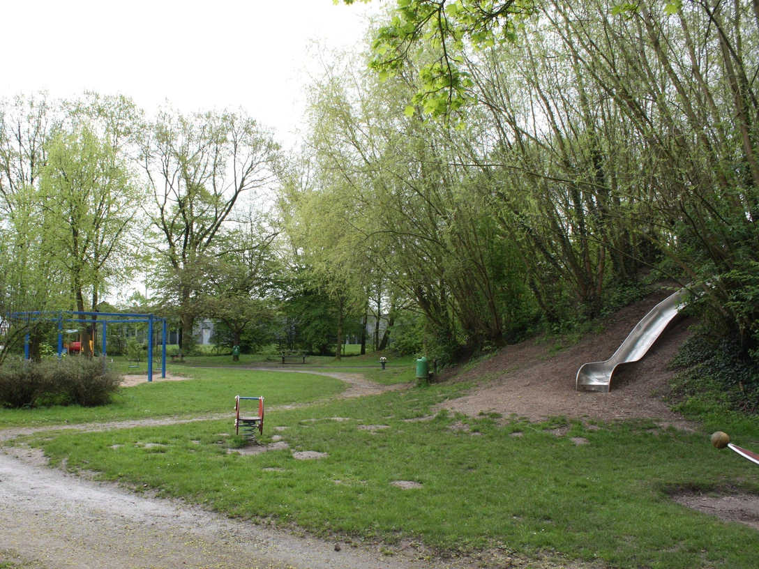 Delbrueck_Abenteuerspielplatz-am-Hallenbad Ein Abenteuerspielplatz mit blauer Kletteranlage, grüner Umgebung und silberner Rutsche am Waldrand.