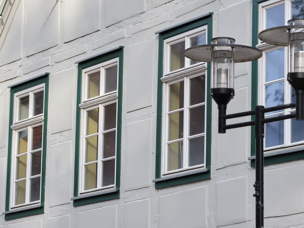 Haus Poelmahn close up Mehrere weiße Fenster mit grüner Umrahmung an einer grauen Fassade neben einer Straßenlaterne.