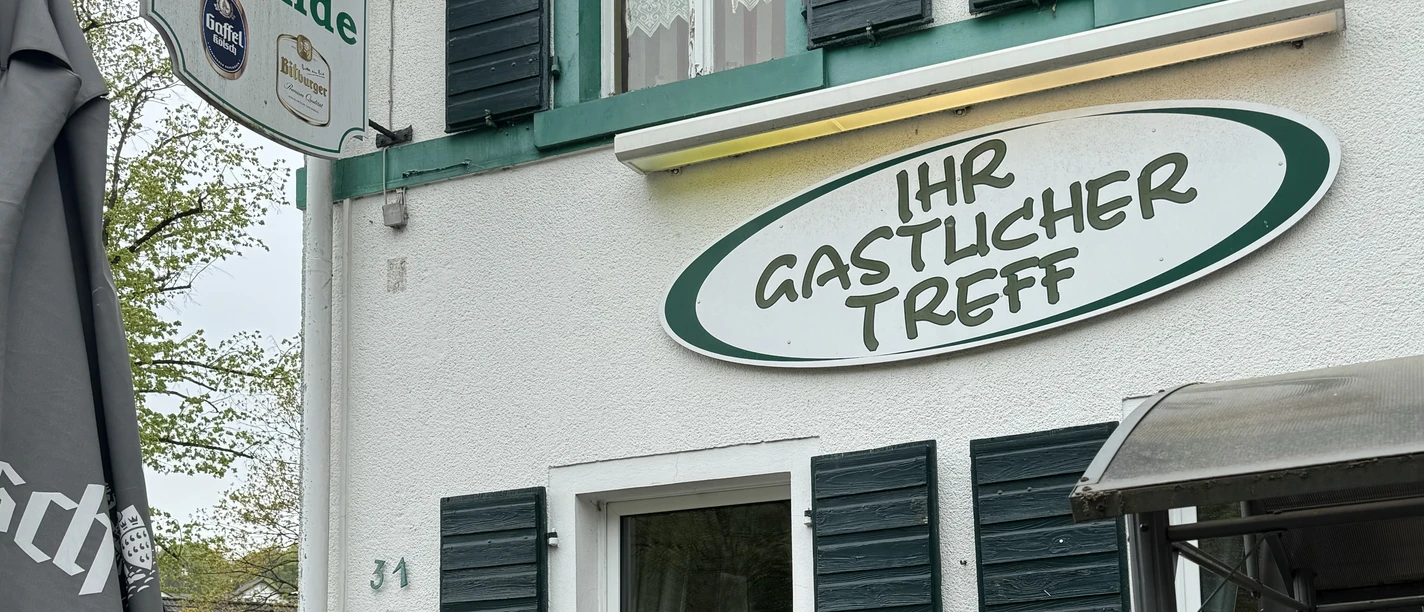 Zur Quelle der Strunde - Außenansicht Gemütliches Gasthaus "Zur Quelle der Strunde" mit grünen Fensterläden und einladendem Eingang.